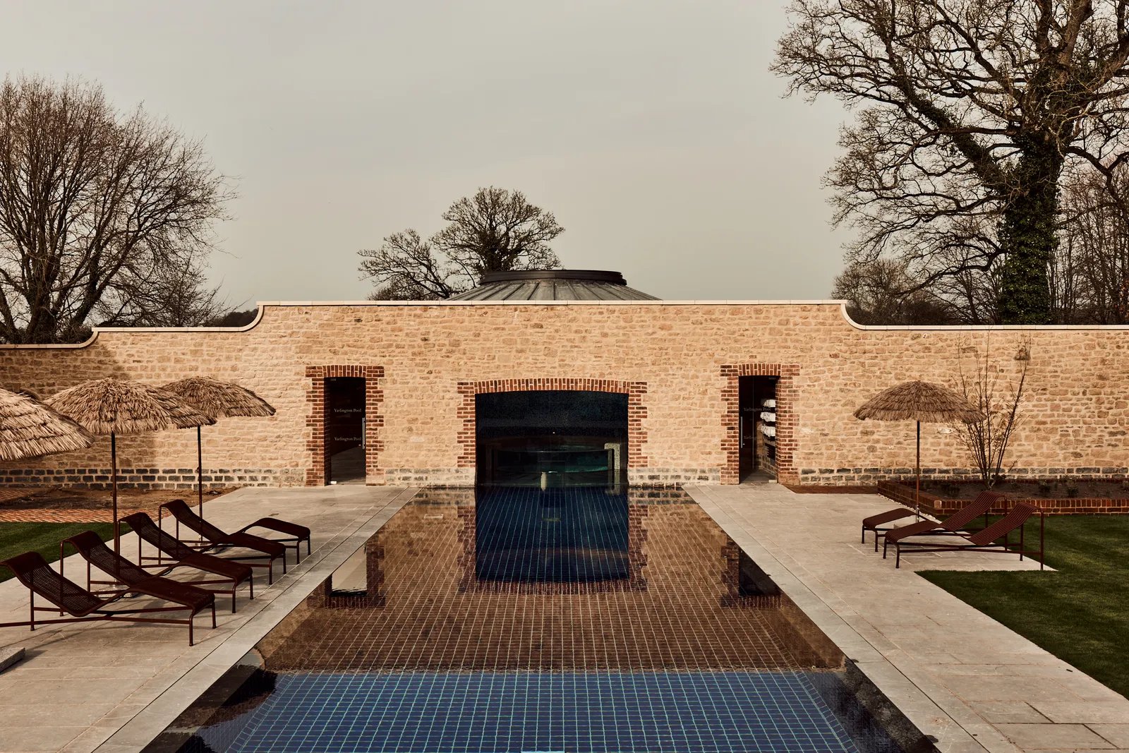 Walled-garden pool with thatched parasols